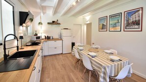 Une cuisine moderne avec un coin repas, comprenant une nappe à rayures, des chaises blanches et un réfrigérateur.