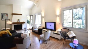 Un salon moderne doté d’une cheminée, de sièges confortables, d’un téléviseur et de grandes fenêtres offrant une vue sur l’extérieur.