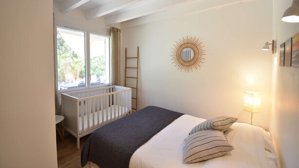 Une chambre avec un berceau, un lit avec des oreillers, un miroir en forme de soleil, une échelle et une fenêtre avec des rideaux.