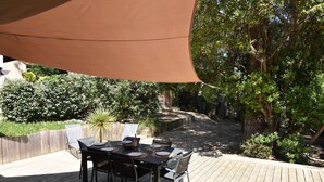 Une terrasse extérieure avec une table dressée pour quatre personnes, entourée d’une plateforme en bois et d’un grand auvent.