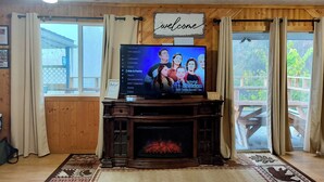 Een woonkamer met een open haard, een televisietoestel waarop 'Young Sheldon' te zien is, en een bord met de tekst 'welkom'.