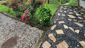 Een tuin met een grote boom, rode bloemen en een pad met staptegels.