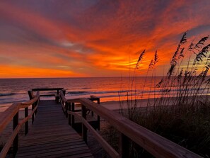 A wooden boardwalk leading to a beach with a sunset in the background. - Vilano Beachside Pool Arcade Theater Slide Firepit (St. Augustine)