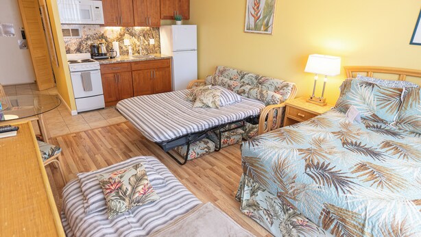 A compact room with a kitchenette, two beds with floral bedding, a small table, and a nightstand with a lamp. - 💎LOCATION💎 5min to 🏄‍♀️🏊‍♀️🐠🦈🌸 free parking 🚙🅿️, fast WIFI💻 🌺F15A07🌺 (Honolulu)