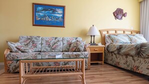 A room with a floral-patterned sofa, a glass-top coffee table, a wooden headboard bed, a nightstand with a lamp, and a framed picture on the wall. - 💎LOCATION💎 5min to 🏄‍♀️🏊‍♀️🐠🦈🌸 free parking 🚙🅿️, fast WIFI💻 🌺F15A07🌺 (Honolulu)
