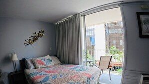 A bedroom with a large bed, a nightstand, a chair, and a view of the outside balcony. - 407 ❤️LOCATION❤️ 5min to 🏄♀️🏊♀️🐠🦈🌸 free parking 🚙🅿️, fast WIFI💻 (Honolulu)