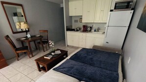 A compact hotel room with a bed, a small dining table with chairs, a kitchen area with cabinets and appliances, and a mirror on the wall. - 407 ❤️LOCATION❤️ 5min to 🏄♀️🏊♀️🐠🦈🌸 free parking 🚙🅿️, fast WIFI💻 (Honolulu)