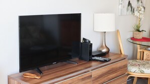 A flat-screen TV on a wooden TV stand, a lamp, a remote control, and a small plant. - free parking 🚙🅿️, fast WIFI💻 🌺2007🌺 (Honolulu)