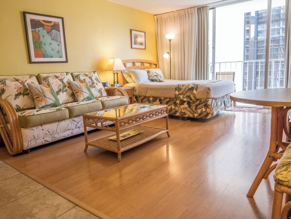 Una habitación de hotel con sofá, cama, una mesita y balcón con vistas a edificios.