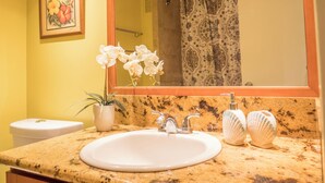 A bathroom with a granite countertop, white sink, and a mirror above it. There is a potted plant and two decorative shells on the counter. - 💎LOCATION💎 5min to 🏄‍♀️🏊‍♀️🐠🦈🌸 free parking 🚙🅿️, fast WIFI💻 🌺F06A07🌺 (Honolulu)