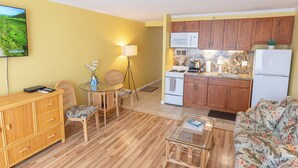 Un espacio habitable compacto con comedor, kitchenette y un televisor mostrando un paisaje hawaiano.