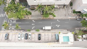 Vista aérea de un estacionamiento con autos, palmeras y un edificio con piscina.