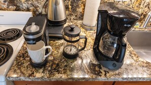Una encimera de cocina con cafetera, hervidor, molinillo de café y un infusor de té.