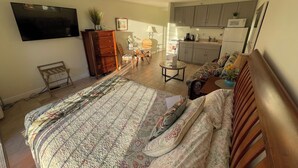 A bedroom with a large bed, a wooden dresser, a TV mounted on the wall, and a kitchenette in the background. - ❤️AWESOME STUDIOS❤️ 5min to 🏄‍♀️🏊‍♀️🏖🐠🐋🦈FREE 🚙🅿️ 250mbps+💻-FREE PARKING (Honolulu)