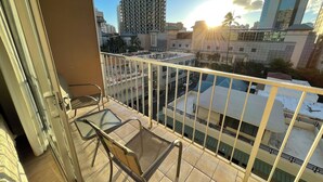 A balcony with a view of a cityscape, including a tall building with a unique facade and palm trees. - ❤️AWESOME STUDIOS❤️ 5min to 🏄‍♀️🏊‍♀️🏖🐠🐋🦈FREE 🚙🅿️ 250mbps+💻-FREE PARKING (Honolulu)