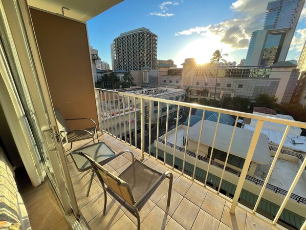 Ein Balkon mit Blick auf eine Stadtlandschaft, darunter ein hohes Gebäude mit einer markanten Fassade und Palmen.