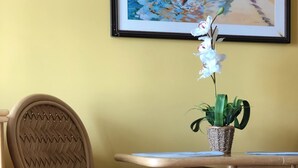 A wicker chair with a cushioned seat and backrest, a small round table, and a potted plant with green leaves and a white flower. - 💎LOCATION💎 5min to 🏄‍♀️🏊‍♀️🐠🦈🌸 free parking 🚙🅿️, fast WIFI💻 🌺F15A06🌺 (Honolulu)