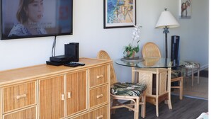 Un salon avec un téléviseur, une table à manger avec des chaises, une lampe et une plante en pot.