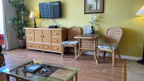 Ein Zimmer mit Fernseher, einem Schrank, zwei Korbstühlen, einem Glastisch und einer Topfpflanze.