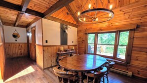 A wooden interior with a round dining table, chairs, a chandelier, and a large window with a view of greenery. - Quiet Luxury, Surrounded by Nature • 5-Star Guest Favorite Near Williamsport, PA (Linden)