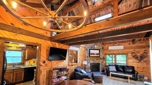 A rustic cabin interior with a wooden dining table, a fireplace, a television, and a stone wall with a mounted picture. - Quiet Luxury, Surrounded by Nature • 5-Star Guest Favorite Near Williamsport, PA (Linden)