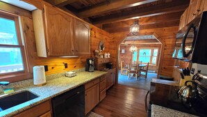 A wooden cabin kitchen with granite countertops, wooden cabinets, a coffee maker, and a dining area with chairs and a table. - Quiet Luxury, Surrounded by Nature • 5-Star Guest Favorite Near Williamsport, PA (Linden)
