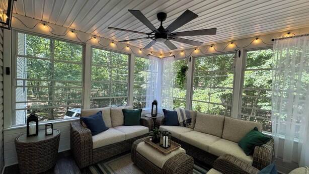Una sala de estar acogedora con ventilador de techo, ventanas amplias, mobiliario de mimbre e iluminación con luces colgantes.