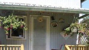 Eine hölzerne Veranda mit Tür, Stuhl und kleinem Tisch.