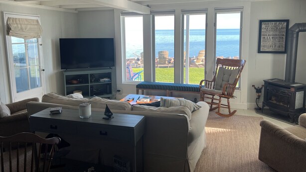 Ein Wohnzimmer mit großem Fenster zum Meer, einem Fernseher und einem Kamin.