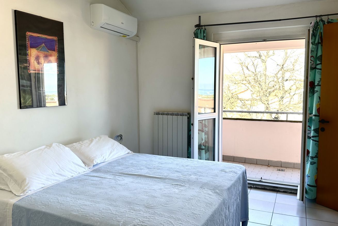 A bedroom with a bed, a radiator, an air conditioner, a sliding glass door to a balcony, and a framed picture on the wall.