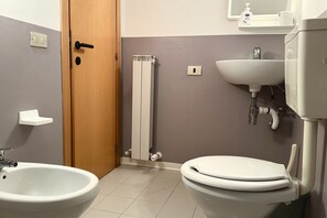 A bathroom with a bidet, a toilet, a sink, and a radiator.