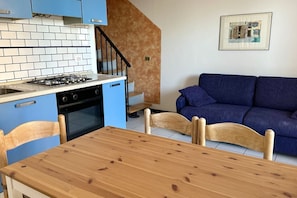 A kitchen with a gas stove, oven, and blue cabinets; a wooden dining table with chairs; a blue sofa; and a staircase with a wooden railing.