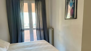 Una habitación con cama, ventana con cortinas, radiador y un cuadro en la pared.