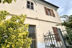 A two-story building with a beige facade, a metal gate, and a number '65' on the wall.