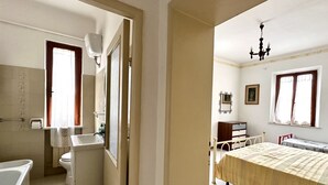 Un dormitorio con cama, mesita de noche, ventana y puerta que da a un baño.
