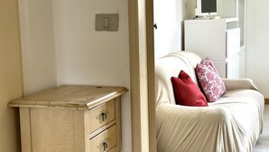 Una habitación con una cama, un tocador, un televisor sobre un mueble bajo y un interruptor de luz en la pared.