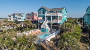A beachfront property with multiple colorful houses, a central swimming pool, and a wooden deck. - Hobbs Realty - "All that Jazz" includes a private pool & panoramic views! (Holden Beach)