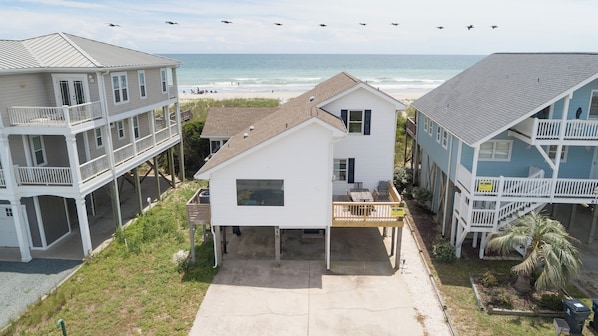 Enjoy ocean views from this beachfront property, featuring a central house with a covered porch and two adjacent buildings.
