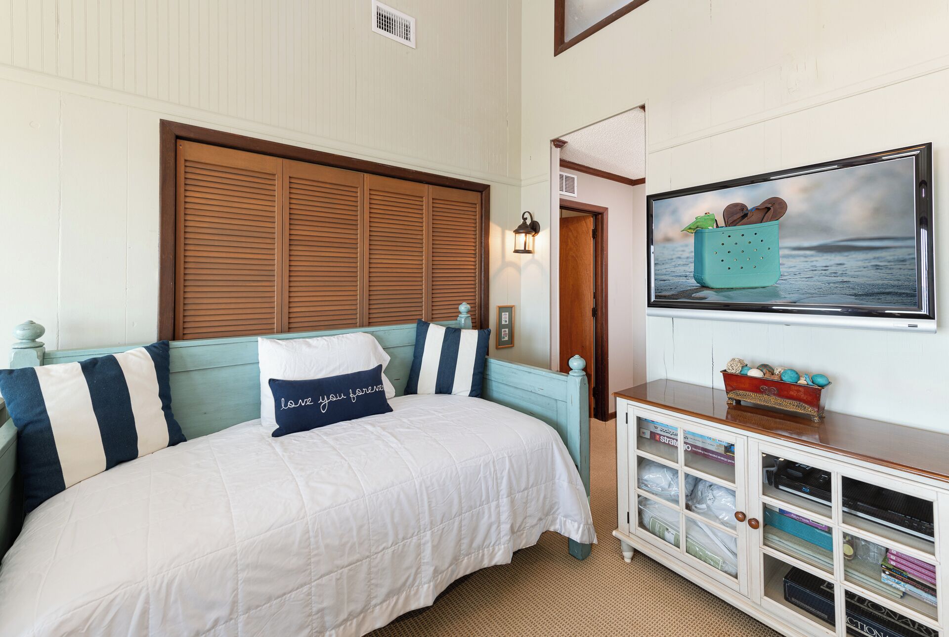 A bedroom with a bed, a wooden headboard, a wall-mounted TV, and a cabinet with storage.