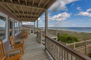 A wooden deck with chairs and a view of the beach.