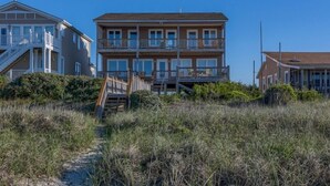 Un edificio frente a la playa con varios balcones y una escalera que lleva a la entrada, bajo un cielo despejado.