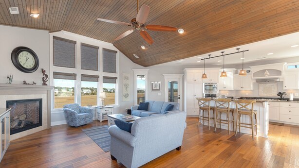 A spacious living room with a fireplace, a large sofa, and a dining area with bar stools. - Hobbs Realty - "Terrapin Station" offer views of the marsh and ocean, 4 bedrooms ,and private pool (Holden Beach)