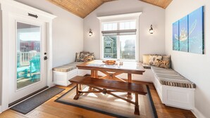 A cozy room with a wooden ceiling, a bench with cushions, a wooden table, and a view of houses through a window. - Hobbs Realty - "Terrapin Station" offer views of the marsh and ocean, 4 bedrooms ,and private pool (Holden Beach)