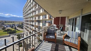 A balcony with wicker furniture, a grill, and a view of a residential area with a mountain in the background. - Quiet, Spotless Condo with King Bed for your Getaway! (Colorado Springs)