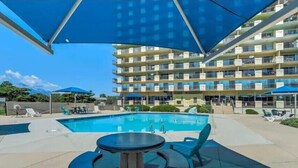 A pool area with a large umbrella, lounge chairs, and a building with multiple balconies in the background. - Quiet, Spotless Condo with King Bed for your Getaway! (Colorado Springs)