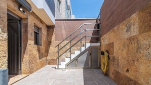 A modern outdoor area with a stone wall, a metal staircase, and a yellow garden hose. - Home2Book Cozy Apt 2 Min From La Garita Beach (La Garita)