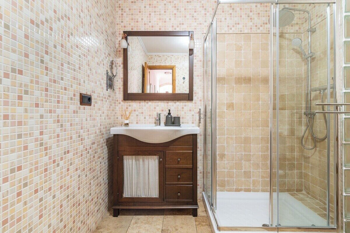 Un bagno con pareti in mosaico, un mobile bagno in legno con specchio e cabina doccia in vetro.