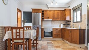 A compact kitchen with wooden cabinets, a built-in oven, and a dining area with a table and chairs. - Home2Book Cozy Apt 2 Min From La Garita Beach (La Garita)