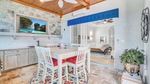 A dining area with a white table and chairs, a patterned rug, and a television displaying a scenic view.