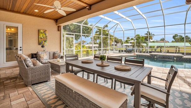 A covered patio with a pool, wicker furniture, and a ceiling fan.